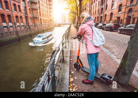 Des profils touriste avec sac à dos sur l'e-scooter profiter plus célèbre quartier des entrepôts de Speicherstadt historique de Hambourg avec rivière et bateau voyage, Ger Banque D'Images