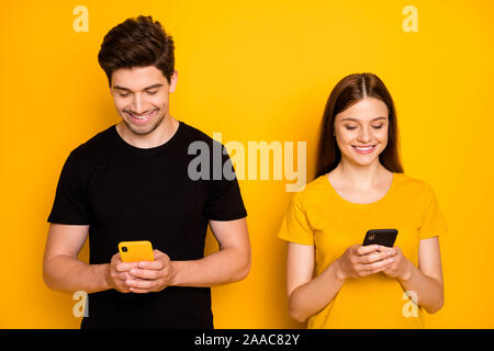 Photo de Happy cute nice positifs toxicomanes la navigation au travers de leur téléphone à discuter les uns avec les autres malgré côte à côte isolée Banque D'Images