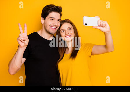 Photo de petit ami et petite amie smiling toothily gaiement voyager autour du monde montrant v-sign en portant des selfies noir T-shirt isolated Banque D'Images