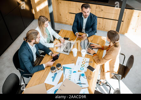 Les gens d'affaires travailler avec les ordinateurs et les statistiques au tableau en bois dans la salle de réunion, voir ci-dessus de la Banque D'Images