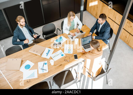 Les gens d'affaires travailler avec les ordinateurs et les statistiques au tableau en bois dans la salle de réunion, voir ci-dessus de la Banque D'Images