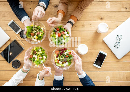 Les employés de bureau au cours d'un déjeuner d'affaires avec des salades et des tasses à café, vue du dessus sur la table en bois Banque D'Images