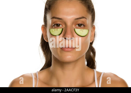 Jeune femme posant avec des tranches de concombres undeer ses yeux sur fond blanc Banque D'Images