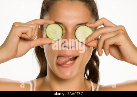 Jeune femme drôle posant avec des tranches de concombres sur les yeux sur fond blanc Banque D'Images