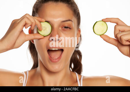 Young smiling woman posing avec des tranches de concombres sur les yeux sur fond blanc Banque D'Images