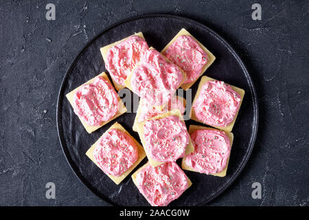 Biscuit surmonté de fraise vanille buttercream frosting parsemé de perles en argent comestibles et de noix de coco râpée sur une plaque noire, vue Banque D'Images