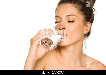 Belle jeune femme boit l'eau du verre sur fond blanc Banque D'Images