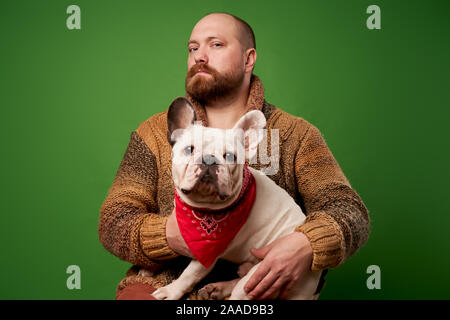 Homme désirant à côté avec bouledogue français dans ses bras sur fond vert vide Banque D'Images