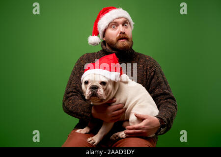 Homme barbu et dog in santa caps sur fond vert en studio vide Banque D'Images