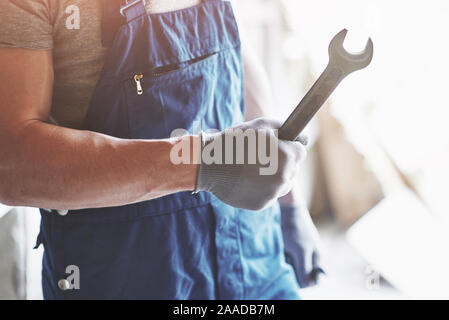 Dans la main avec des gants un métal clé sur un arrière-plan d'un costume du travailleur en usine. Banque D'Images