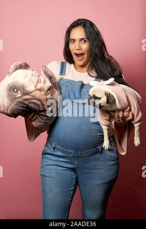 Jeune brunette avec pug et oreiller dans ses mains vides sur fond rose en studio Banque D'Images