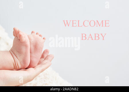 Invitation à une fête en blanc. Carte de douche de bébé. Les jambes de bébé sur la main de maman close-up. Copier l'espace. Place pour le texte. Banque D'Images