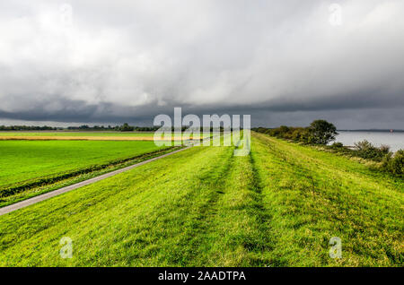 Des nuages sombres sur un vaste paysage sur l'île de Schouwen-Duiveland, aux Pays-Bas, avec une digue herbeuse, champs verts et le lac de Grevelingen Banque D'Images