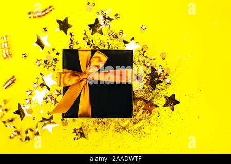 Boîte cadeau noire avec archet d'or sur fond jaune avec des paillettes. Maison de concept. Banque D'Images