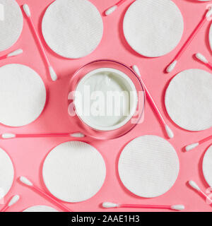 Produits d'hygiène : rond blanc coton et bâtons en plastique pour nettoyer les oreilles se trouvent sur un fond rose à côté de la crème pour le visage Banque D'Images