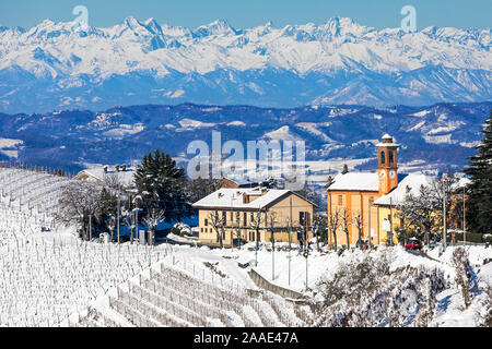 Maison rurale et église paroissiale entre vignobles couverts dans la neige des montagnes enneigées sur contexte en Piémont, Italie du Nord. Banque D'Images