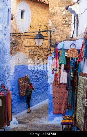 Un propriétaire de boutique marocaine locale se bloque ses articles à l'un des murs bleus de Chefchauen, la ville bleue dans les montagnes du Maroc dans un matin d'automne. Banque D'Images