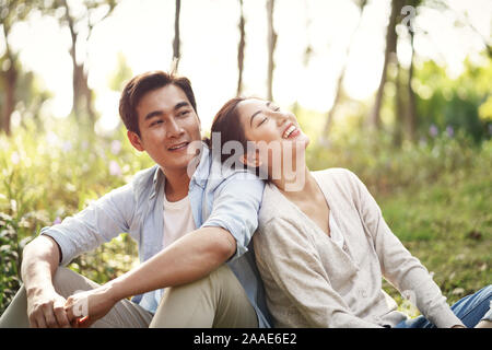 Beautiful happy young asian woman sitting on grass talking chatting relaxing in park Banque D'Images