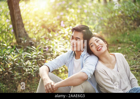 Beautiful happy young asian woman sitting on grass talking chatting relaxing in park, high angle view Banque D'Images