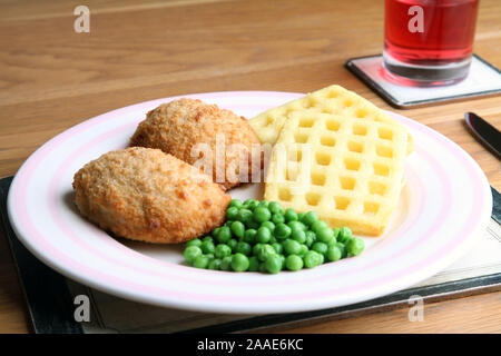 Chicken ensemble avec des gaufres de pommes de terre et les pois sur la plaque a servi à table avec des couverts et un verre de Cassis dans verre Banque D'Images