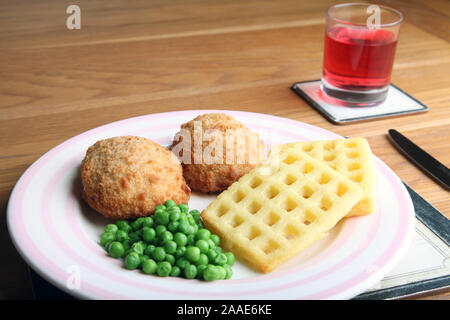 Chicken ensemble avec des gaufres de pommes de terre et les pois sur la plaque a servi à table avec des couverts et un verre de Cassis dans verre Banque D'Images