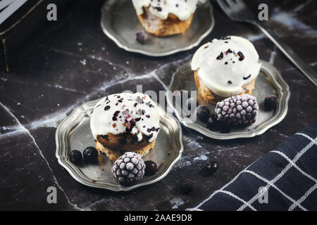 De délicieux muffins aux bleuets avec glaçage au chocolat blanc décorée sur les plateaux en étain avec des baies sur backgrund de marbre noir Banque D'Images
