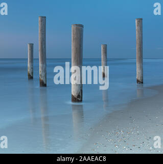 Cinq poteaux en bois historiques pendant le coucher du soleil des temps d'exposition, plage de Petten, Pays-Bas Banque D'Images