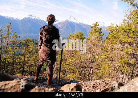 Une jeune femme avec un bâton de marche canne acier fixant l'enneigés des montagnes de Tantalus et arbres résineux vert Banque D'Images