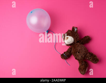 Petit ours en peluche brun tenant un ballon bleu sur une corde sur un fond rose Banque D'Images