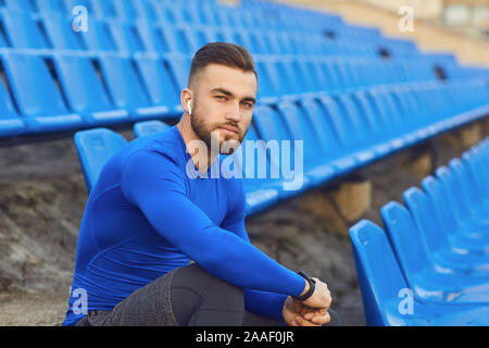 Un gars en sportswear est assis dans le stade après la formation. Banque D'Images