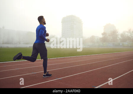 Un jeune athlète exécute sur un stade dans le brouillard. Banque D'Images