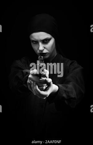 Jeune fille sérieuse avec arme visant à huis clos sur fond noir, monochrome Banque D'Images