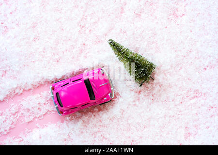 Petit jouet voiture enfants et vert sapin de Noël couvert de neige artificielle rose Banque D'Images
