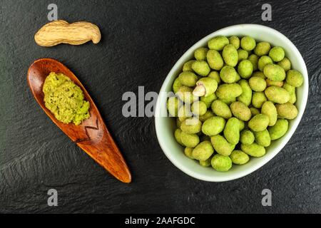 Arachides enrobées de wasabi sur ardoise. Wasabi japonais d'épices. Wasabi vert arachides sur une plaque noire sur un fond sombre. Banque D'Images