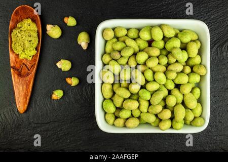 Arachides enrobées de wasabi sur ardoise. Wasabi japonais d'épices. Wasabi vert arachides sur une plaque noire sur un fond sombre. Banque D'Images