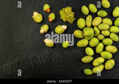 Arachides enrobées de wasabi sur ardoise. Wasabi japonais d'épices. Wasabi vert arachides sur une plaque noire sur un fond sombre. Banque D'Images