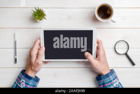 Comprimé dans la main sur la maquette d'un bureau. Vue de dessus, fixer la composition. Close-up. Bureau en bois blanc. Banque D'Images