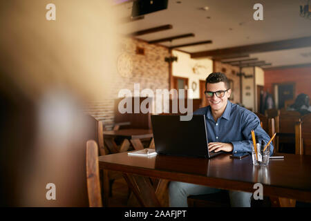 Portrait authentique de young smiling businessman looking at camera with laptop in cafe. Hipster comme l'Homme à lunettes élégant et smart casual shirt Banque D'Images