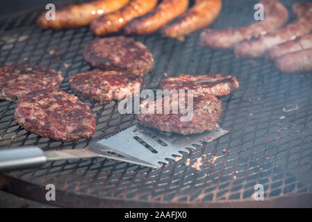 Spatule en acier basculant un pâté d'hamburger est cuit sur un grill ouvert Banque D'Images