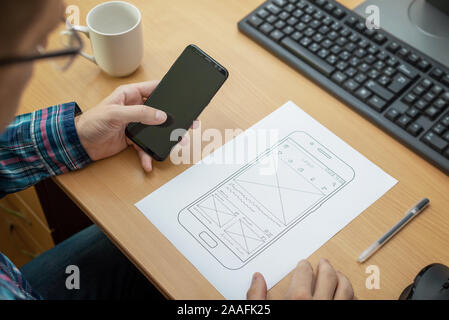 Designer dessins le mise en page d'un site sensible ou l'app et les teste sur un téléphone mobile. Close up, un bureau avec ordinateur à côté. Banque D'Images