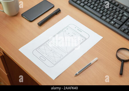 Esquisse d'un site web ou téléphone mobile app sur wireframe. Sur le bureau. Keyobard, stylo, téléphone, café et la loupe à côté. Close up. Banque D'Images