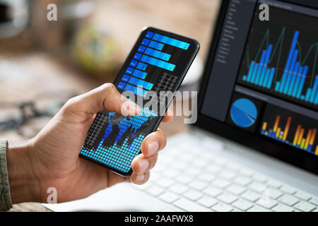 Close-up d'un courtier en bourse à l'aide de téléphone mobile avec le graphique sur écran Banque D'Images