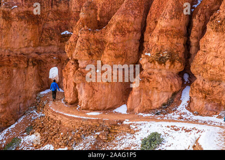 Jeune femme en veste bleue marchant à travers un tunnel le long du sentier des roches rouges après la neige fraîche. Banque D'Images