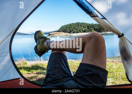 La première personne d'un homme a les jambes croisées à l'entrée d'une tente sur l'île de Skagit, Washington, USA. Banque D'Images