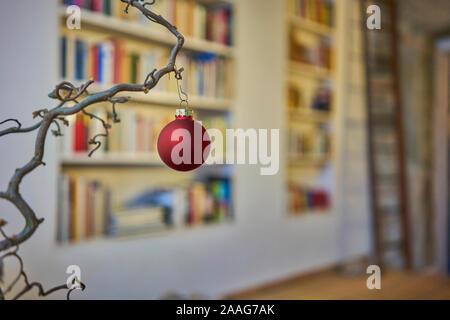 Close up of red boule de noël à une branche en face de l'arrière-plan flou de bookshelf Banque D'Images