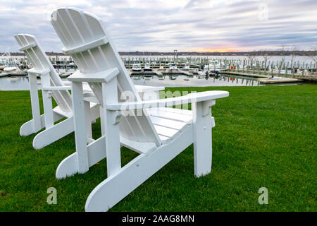 'Blanc' style Adirondack chaises de salon sur l'herbe verte au waterfront marina, avec des bateaux amarrés en arrière-plan Banque D'Images