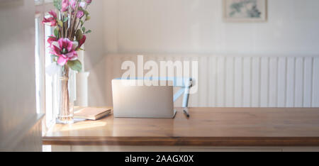 Gros plan de travail confortable avec des maquettes, des fournitures de bureau de l'ordinateur portable et rose flower vase sur table en bois en regard de windows Banque D'Images