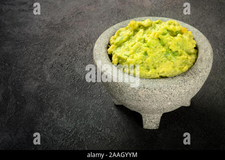 Le guacamole dans un molcajete, avocat mexicain sauce trempette dans le mortier traditionnel en pierre, sur un fond noir avec copie espace Banque D'Images