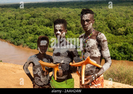 L'Éthiopie, de l'Omo, Kolcho habillé traditionnellement Village les jeunes hommes de la tribu Karo au-dessus de la rivière de l'Omo en bois fait main tenant à vendre aux touristes des tabourets Banque D'Images