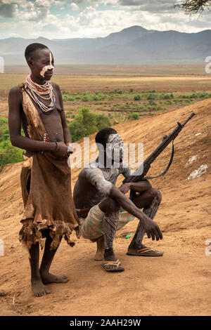 L'Éthiopie, de l'Omo, Kolcho, village tribal Karo man holding, fusil à verrou avec femme décorée de la boue, au-dessus de la rivière Omo Banque D'Images